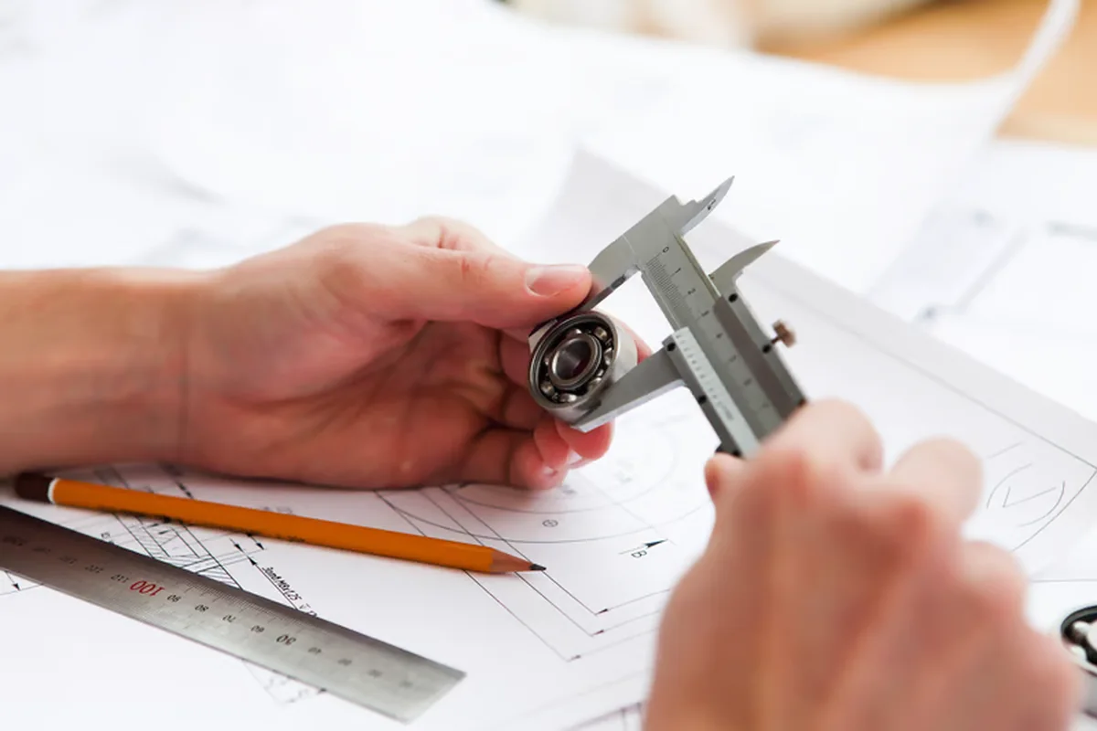Engineer measuring a mechanical component with calipers over an engineering drawing